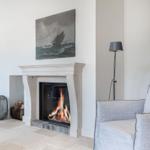 Fireplace with burning fire, gray sofa, and wall painting with sailboat.