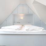 Doppelbett unter Dachschräge mit integrierten Schränken und Nachttischbeleuchtung.