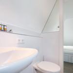 Badezimmer mit Waschbecken, Spiegel und Toilette. Blick in Schlafzimmer mit Bett.