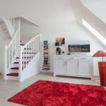 Wohnzimmer mit rotem Teppich, weißer Treppe und Fernseher auf Schrank.