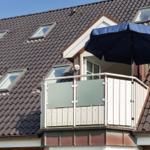Terrasse mit blauem Sonnenschirm und Glasgeländer an Haus mit Dachfenstern.