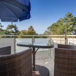 Terrasse mit Tisch, Stühlen und Sonnenschirm. Blick auf Bäume und Himmel.
