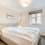 Bedroom with double bed, two nightstands, and window overlooking buildings.