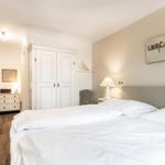 Bedroom with double bed, white closets, and wooden floor.