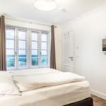 Bedroom with sea view, white bed, windows, and wall picture.