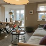 Living and dining area with sofa, table, and chairs. Kitchen in the background.