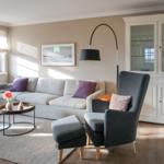 Living room with sofa, armchair, and glass cabinet. Wooden floor and window with roller shades.