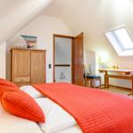 Schlafzimmer mit Dachschrägen, Bett, Schrank, Schreibtisch und Sofa.