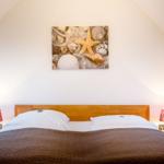 Schlafzimmer mit Bett, Nachttischen und Wandbild mit Muscheln und Seestern.