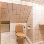 Bad mit Toilette, Waschbecken und Holzregal. Dachschrägen Decke und Fliesenwand.