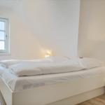 Bedroom with white bed, nightstand, and window.
