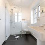 Bathroom with shower, sink, and toilet. Window provides daylight.