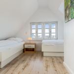 Two single beds with nightstand and window in attic room.