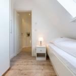 Bedroom with sloped ceiling, white bed and nightstand. Wooden floor and wardrobe.