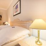 A bed with white linens, nightstand with lamp and wall art.