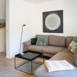 Wohnzimmer mit grauem Sofa, Tisch und Wandbildern.
