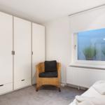 Schlafzimmer mit Bett, Kleiderschrank und Sessel vor Fenster.