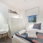 Schlafzimmer mit Bett, Kleiderschrank und Stuhl. Fenster mit Rollladen und Pflanze.