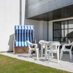 Terrasse mit weißem Tisch, Stühlen und Strandkorb mit blau-weißem Streifen.