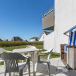 Terrasse mit weißem Tisch und Stühlen, Strandkorb und Blick auf Grünfläche und Häuser.