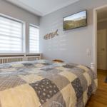 Schlafzimmer mit Bett, TV und Fenstern mit Jalousien.