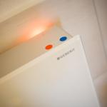 Weiße Toilettenkabine mit orangefarbenem Licht und blau-orangefarbenen Markierungen.