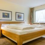 Schlafzimmer mit Holzbett, Nachttisch und Fenster mit Vorhängen.