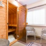 Sauna mit Holzwand, Sitzbänken und zwei Stühlen vor Fenster.