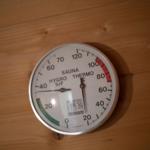 Sauna-Thermometer an Holzwand montiert, zeigt Temperatur und Luftfeuchtigkeit an.