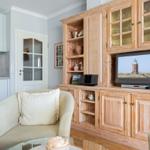 Wohnzimmer mit Holzregal, Fernseher und Sitzgelegenheit. Küche im Hintergrund.