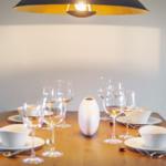 Holztisch mit weißen Tellern, Gläsern und einem weißen Vase unter einer Lampe.