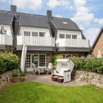 Haus mit Balkonen, Terrasse und Garten. Ein Strandkorb steht auf dem Hof.