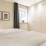 Schlafzimmer mit Bett, Kleiderschrank und Fenster mit Vorhang.