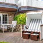 Terrasse mit Gartenliege, Tisch und Stühlen vor Haus mit Holzveranda.