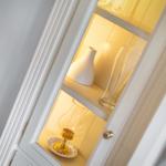 Weißer Schrank mit beleuchteten Regalen und Glasgegenständen.
