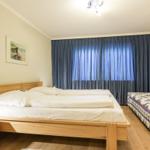 Zimmer mit Doppelbett und Einzelbett, blauen Vorhängen und Holzmöbeln.