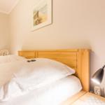 Ein Bett mit weißer Bettwäsche, Holzkopfteil, Stehlampe und Wandbild.