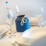 Tisch mit weißen Tellern, Gläsern und blauem Vasenobjekt.