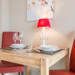 Wooden table with two red chairs, placemats, glasses, and a red lamp.