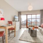 Living and dining area with balcony, sofa, dining table, and TV.