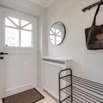 Entrance with white door, round mirror, and hooks for bags.