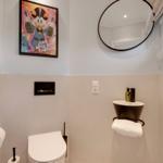 Bathroom with toilet, sink, and wall mirror. Wall art and towel holder visible.