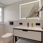 Bathroom with sink, mirror, and toilet. Window and modern fixtures.