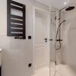 Modern shower with glass enclosure and black fixtures. White walls and sink.