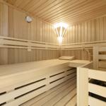 Sauna with wooden bench, stove, and thermometer on the wall.