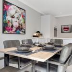 Dining table with chairs, wall art, and kitchen area.
