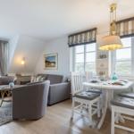 Living and dining area with sofa, chairs, and table. Large windows with view of landscape.