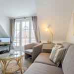 Living room with sofa, armchair, glass table, and TV. Window with view of house.