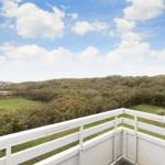 White balcony with view of green meadows and hills under blue sky with white clouds.