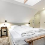 Schlafzimmer mit Doppelbett, Holzbank und Nachttisch unter Dachschrägen.